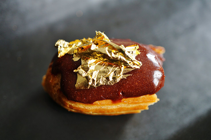 A small eclair with edible gold on top.