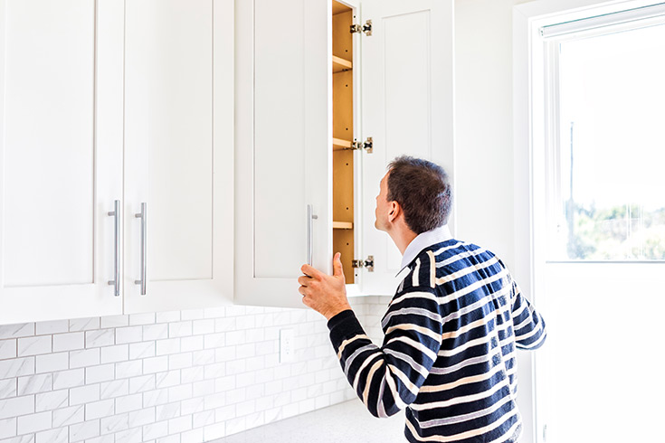 A young man looking inside an empty pantry cabinet.