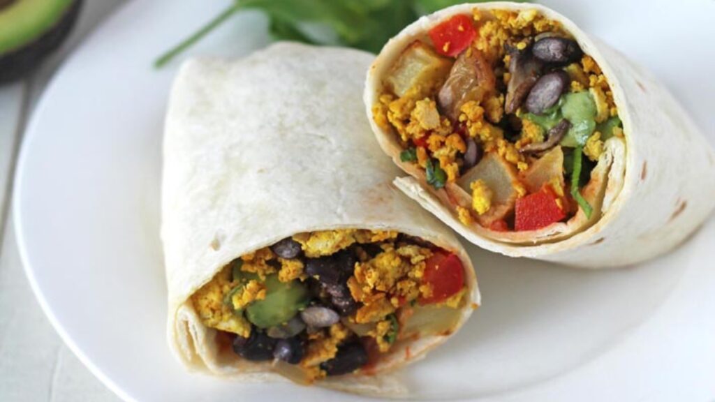 A cut vegan breakfast burrito on a white plate.