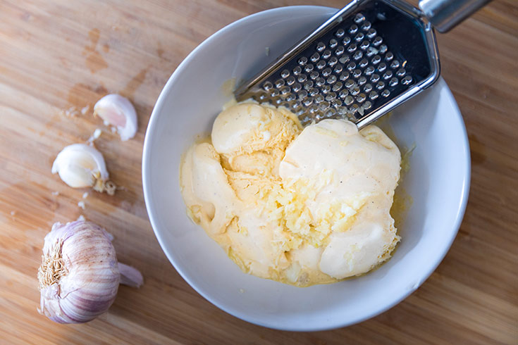 Vanilla ice cream in white bowl with garlic and grater on wooden table.