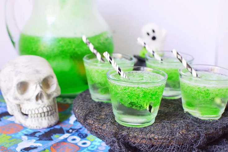 Clear cups with straws sit filled with green goo next to a skull.