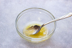 Dressing for this Grape Salad Recipe mixed in a clear, glass mixing bowl. A spoon rests in the bowl.