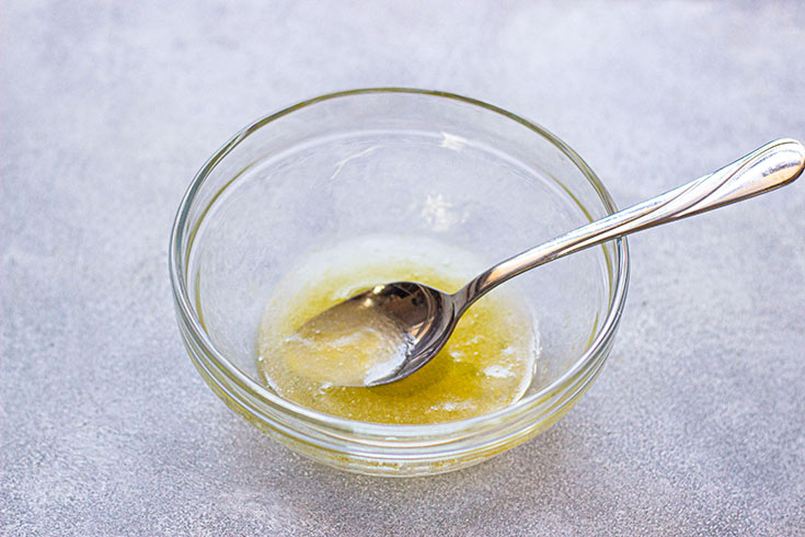 Dressing for this Grape Salad Recipe mixed in a clear, glass mixing bowl. A spoon rests in the bowl.