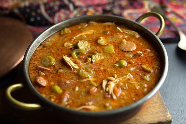A bowl of gumbo sits on a cutting board.