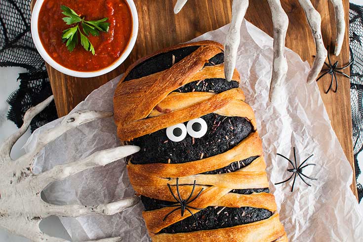 A Stromboli made to look like a mummy lays on a cutting board.