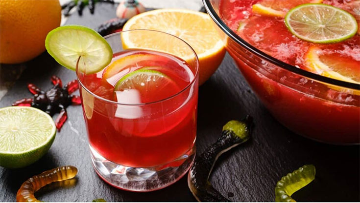 A cup next to a punch bowl. Both container hocus pocus punch and are garnished with citrus slices.