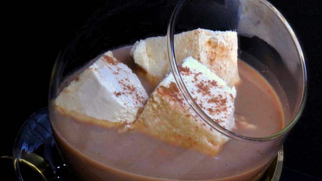 A brandy glass on a warmer, filled with hot chocolate and three square marshmallows.