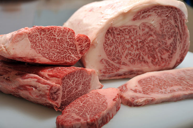 Raw kobe beef laying on a white cutting board.
