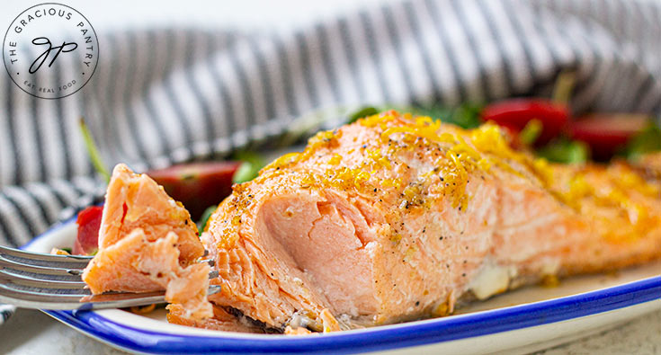 A fork flakes away a portion of salmon from a fillet on a plate.