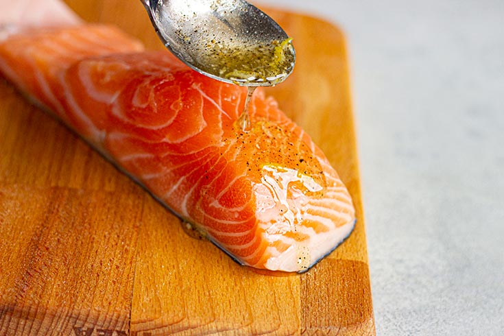 Spooning lemon butter sauce over a raw salmon fillet.