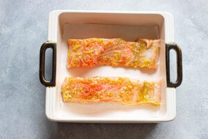 Raw lemon salmon fillets in a baking dish.