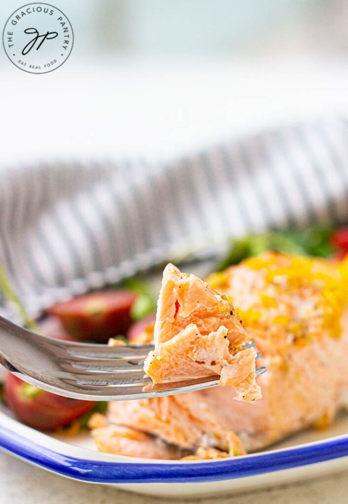 A fork lifts a bite of salmon from a fillet on a plate.