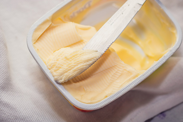 A knife scraping some margarine out of a container.