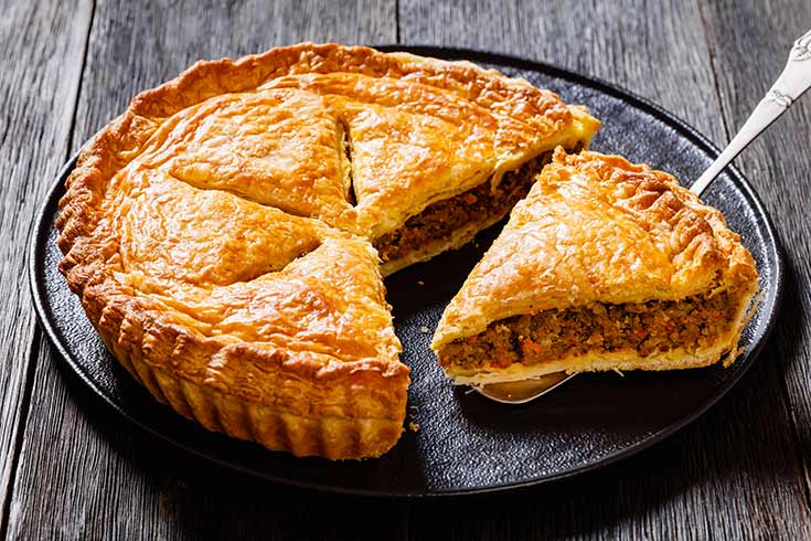 A meat pie with a slice sitting on a spatula next to the cut pie.