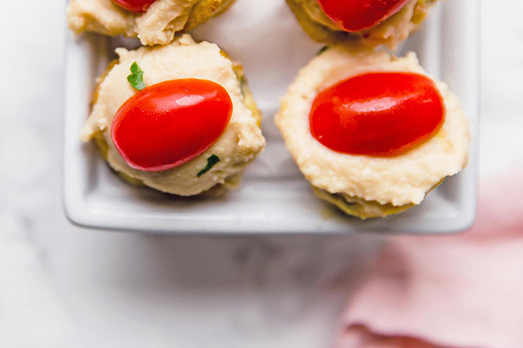 An overhead view of four mini quiches topped with hummus and a half a grape tomato.