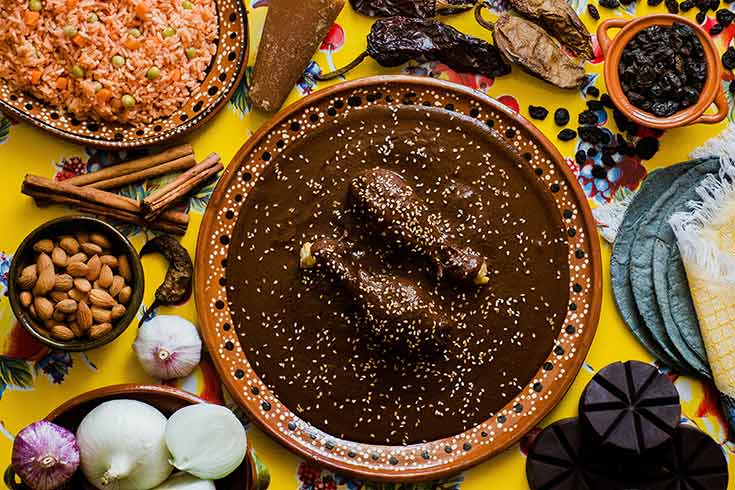 An overhead view of a plate of Mexican mole surrounded by various ingredients and sides.