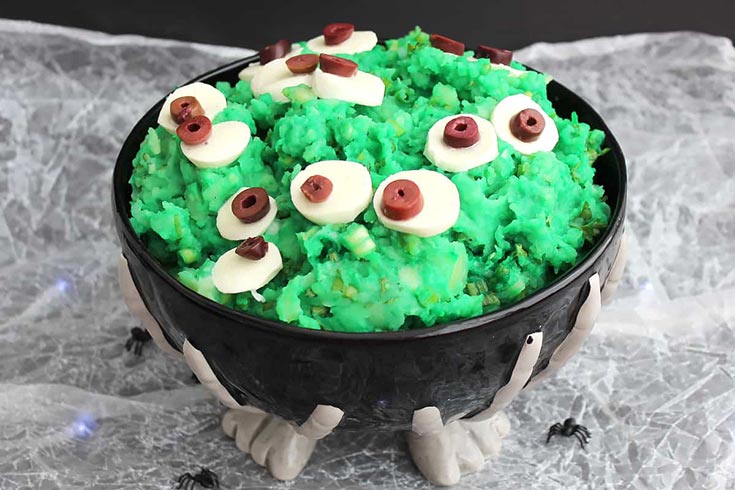 A bowl of green mashed potatoes in a black halloween bowl.