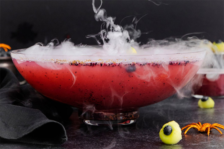 A punch bowl filled with halloween punch with smoke coming off of the tope.