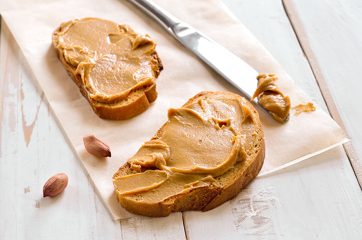 Two slices of bread on a tabletop with nut butter spread on them.