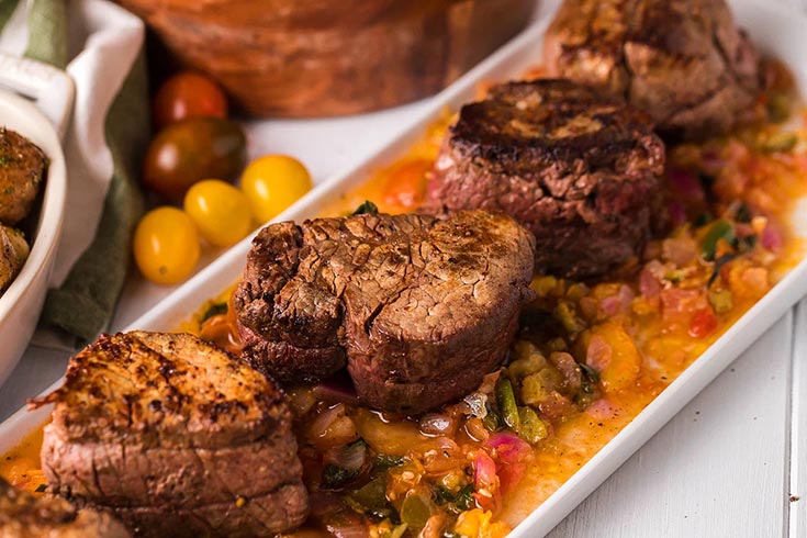 A white platter holds stacks of pan roasted beef tenderloin medallions with tomato relish.