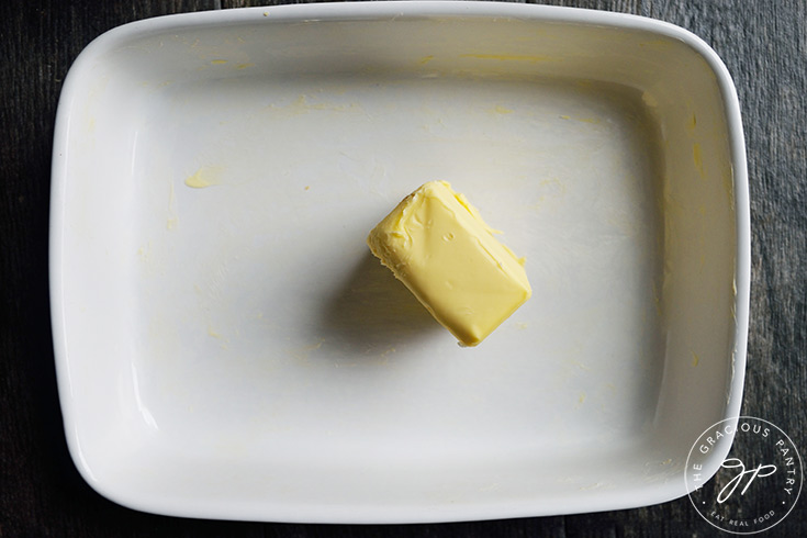 A cube of butter in a buttered baking dish.
