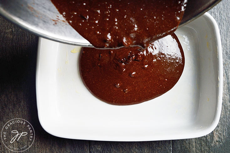 Pouring Peanut Butter Swirl Brownie batter into a buttered casserole dish.