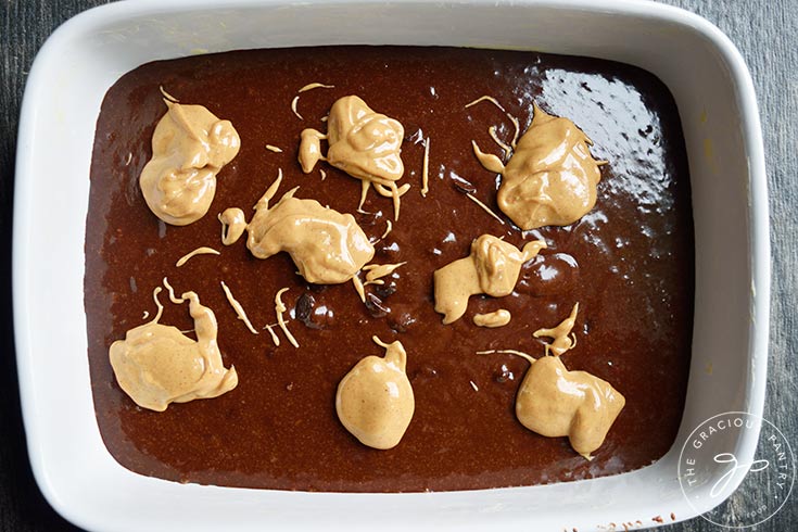 Dollops of peanut butter mix dropped over the brownie batter in a baking dish.