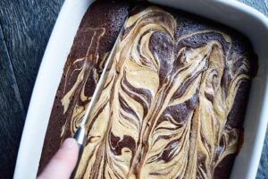 Cutting Peanut Butter Swirl Brownies in a casserole dish.