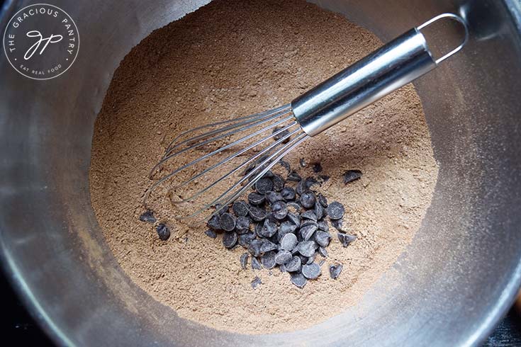 Chocolate chips added to dry ingredients in a mixing bowl.