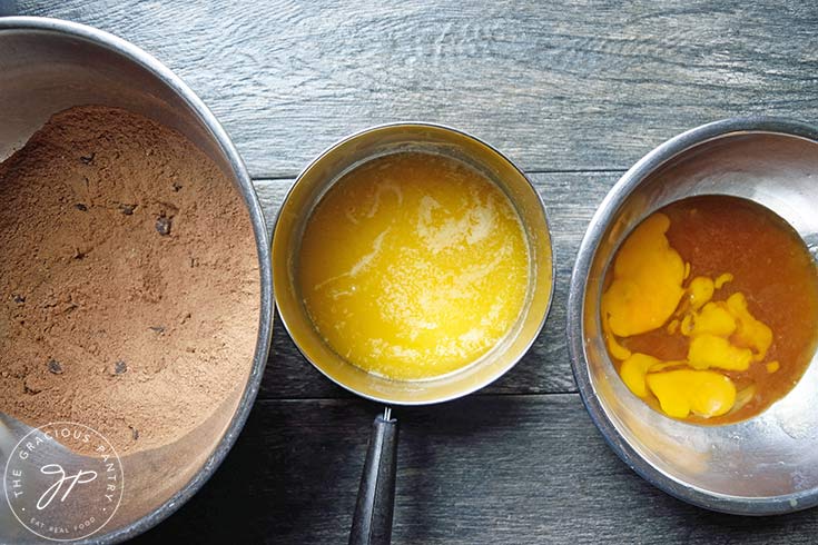 A mixing bowl of dry flour mix on the left, a small pot of melted butter in the middle and a mixing bowl of wet ingredients on the right.