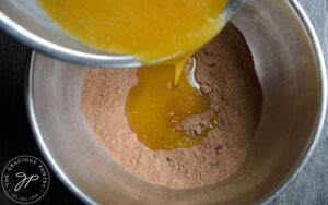 Pouring wet ingredients into dry ingredients in a large, metal mixing bowl.