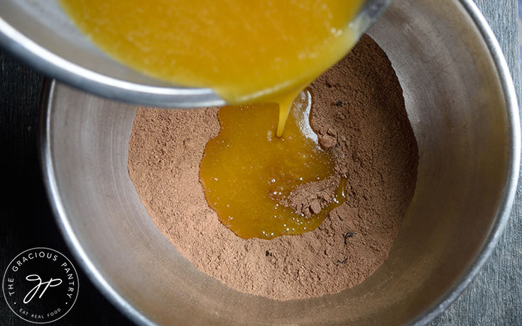 Pouring wet ingredients into dry ingredients in a large, metal mixing bowl.