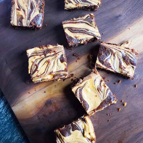 Several Peanut Butter Swirl Brownies spread out over a dark wood cutting board.