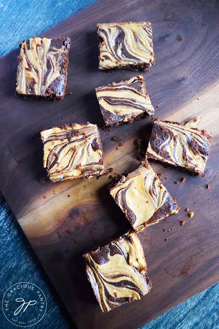 Several Peanut Butter Swirl Brownies spread out over a dark wood cutting board.