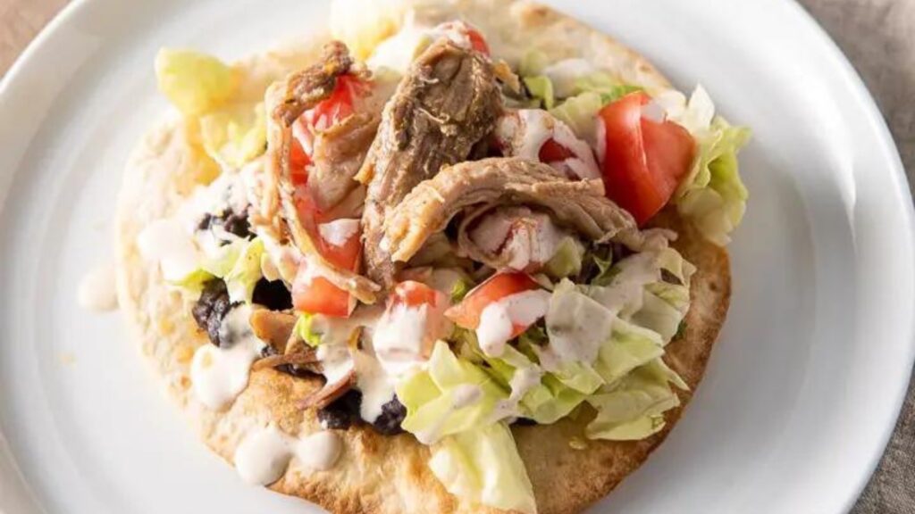 A closeup of a pulled pork tostada on a white plate.