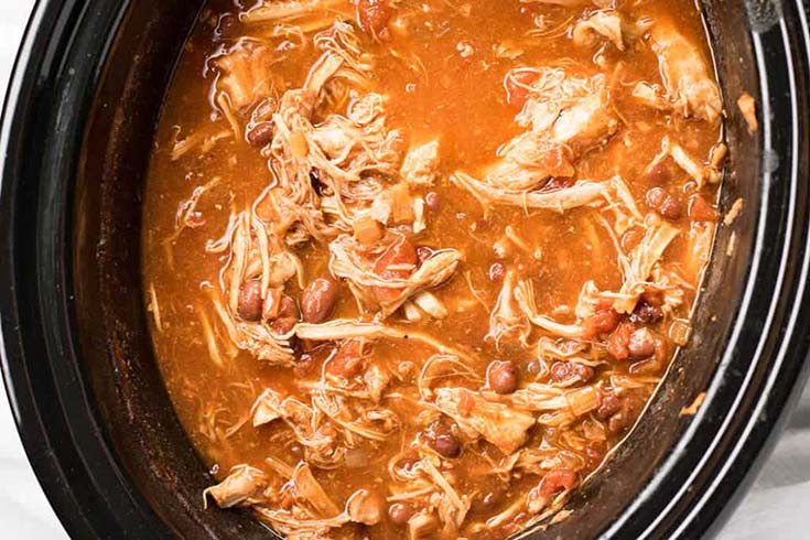 An overhead view of pulled pork chili in a black slow cooker crock.