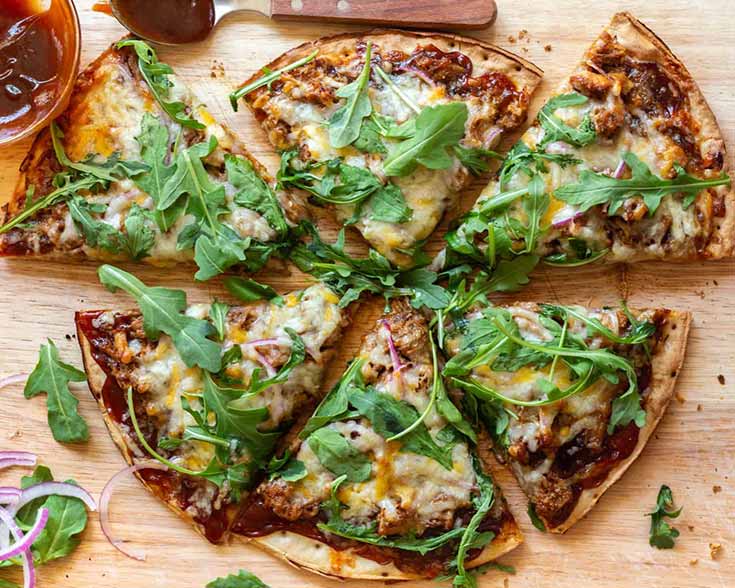 An overhead view of a cut, pulled pork pizza on a cutting board.