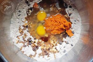 Egg, pumpkin and other wet ingredients added to a mixing bowl with flour mixture in it.