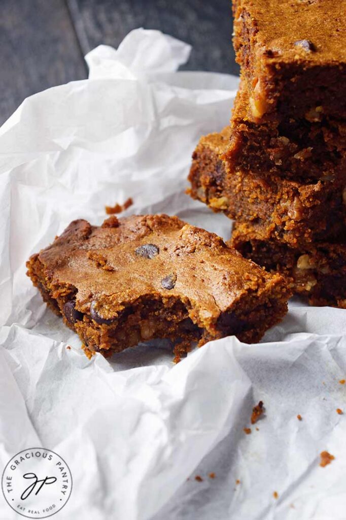 A single Pumpkin Blondie with a bite removed sits on parchment next to a stack of blondies.