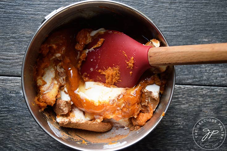 Recipe ingredients partially mixed in a mixing bowl with a red spatula.