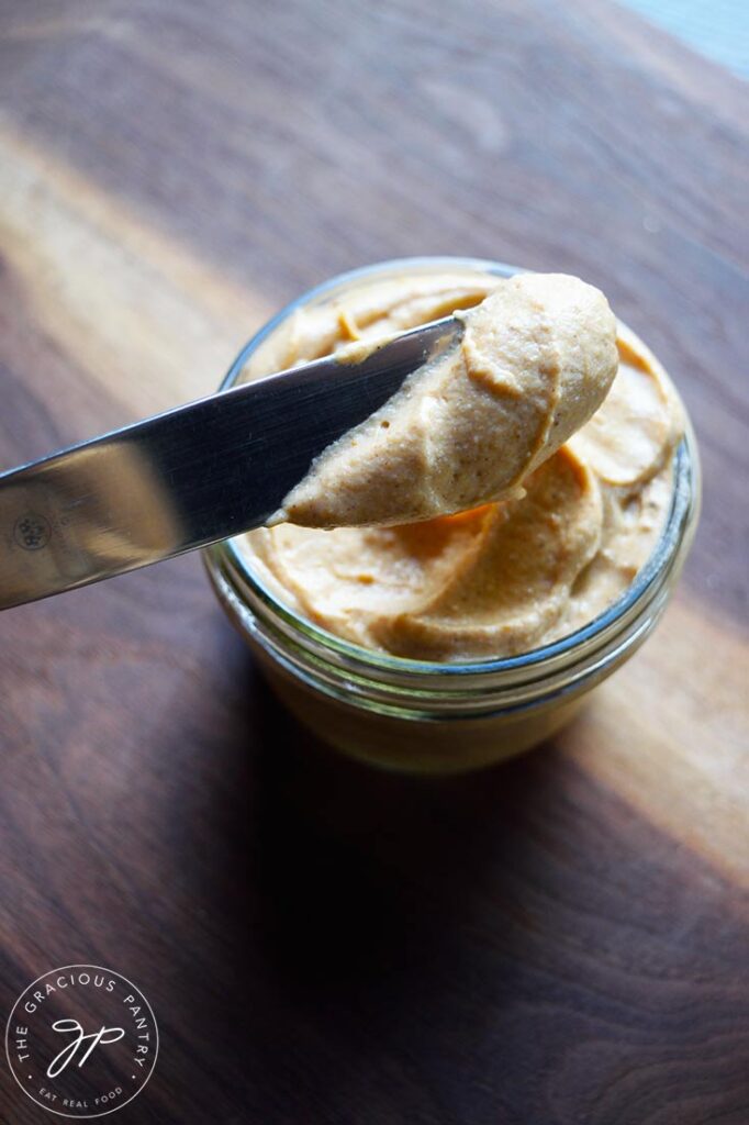A knife scoops a dollop of pumpkin cream cheese out of a jar full of it.