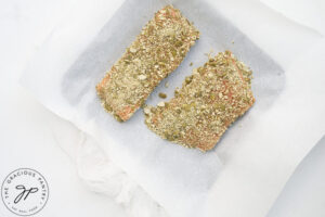 Two fillets of Pumpkin Seed Crusted Salmon on a parchment-lined baking sheet.