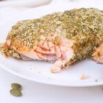 A Pumpkin Seed Crusted Salmon fillet on a plate with a bite missing.