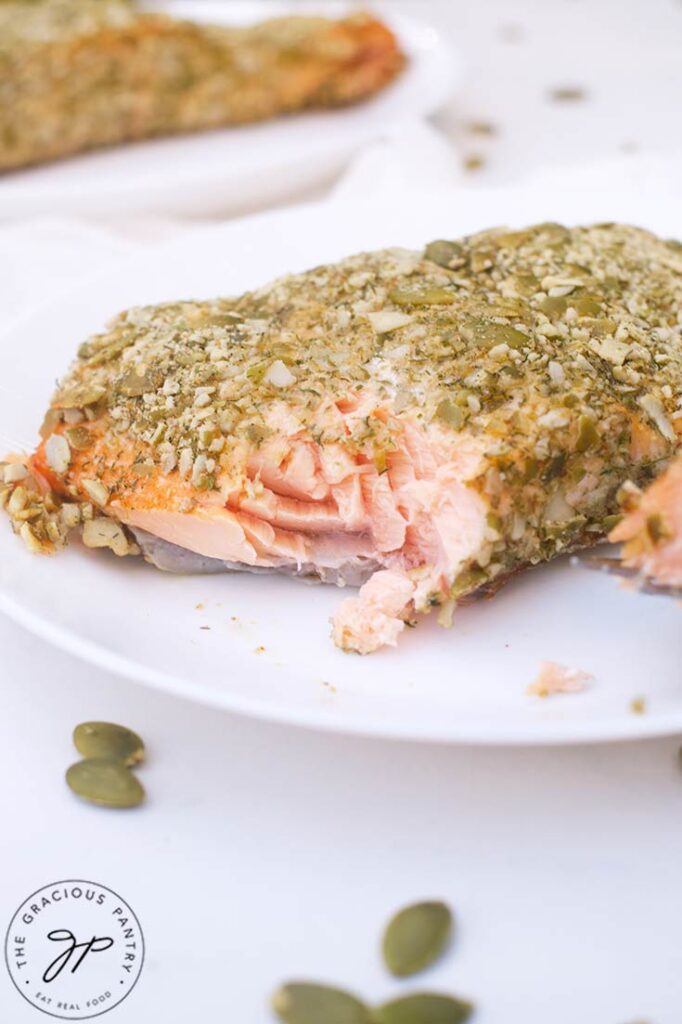 A Pumpkin Seed Crusted Salmon fillet on a plate with a bite missing.