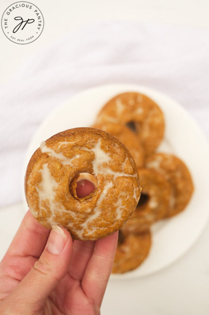 A female hand holds up a pumpkin donut over a plate full of them.