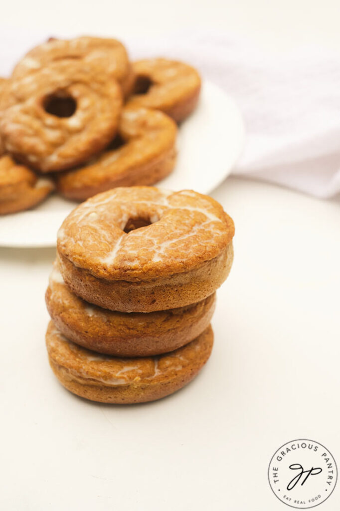 A stack of Pumpkin Donuts sits in front of a plate full of them.