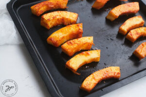 Baked Pumpkin Fries on a baking sheet, cooling on a white surface.