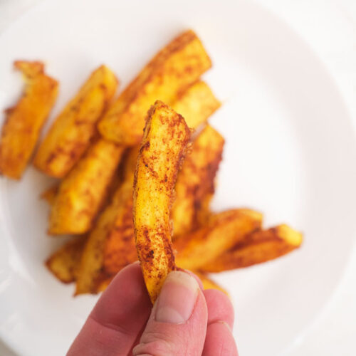 A hand holds up a single Pumpkin Fry over a plate filled with them.