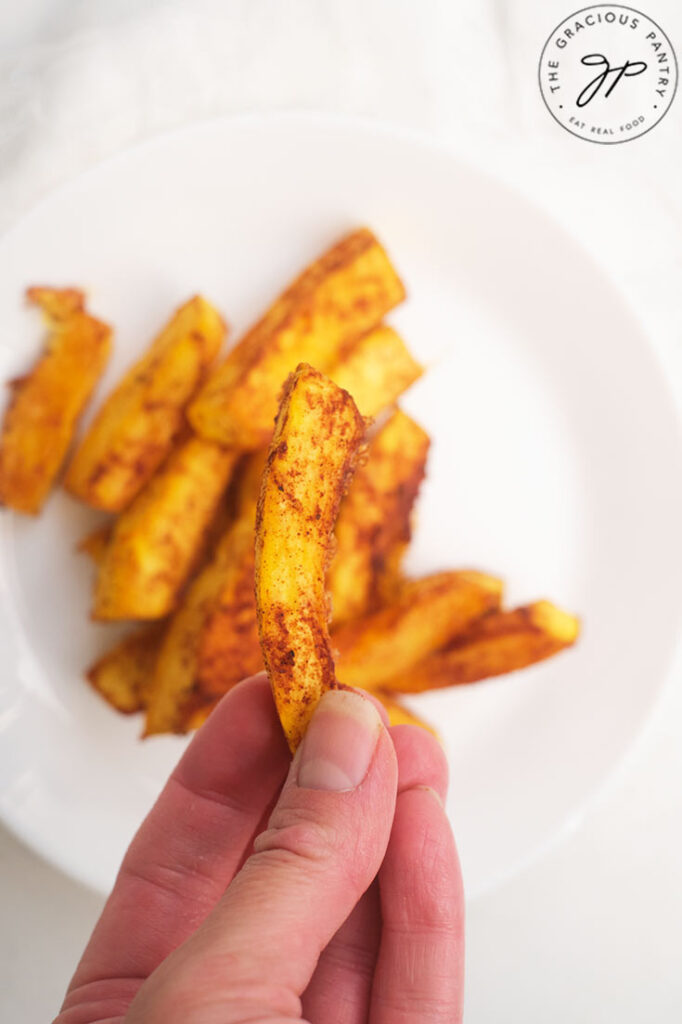 A hand holds up a single Pumpkin Fry over a plate filled with them.