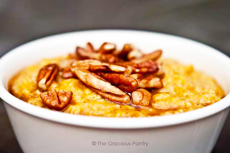 A white bowl holds a serving of pumpkin pie oatmeal and is topped with pecans and maple syrup.